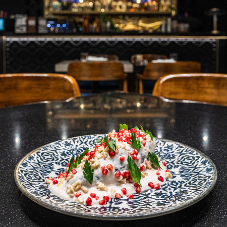 Chile en nogada servido en plato decorado con crema de nuez, granada fresca y perejil en restaurante elegante.