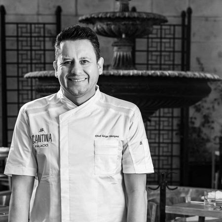 Chef sonriendo en comedor elegante con fuente decorativa al fondo en ambiente blanco y negro.