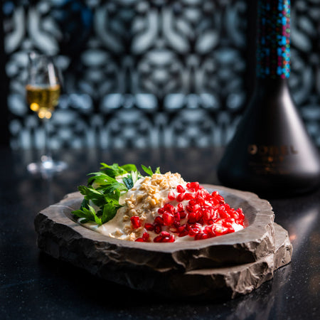 Chile cubierto de nogada con granada fresca y hierbas servido sobre piedra oscura en ambiente elegante.