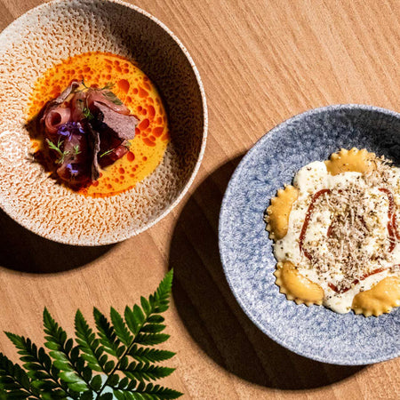 Ravioles con salsa cremosa y queso rallado junto a carpaccio en caldo rojo con brotes y flores comestibles.